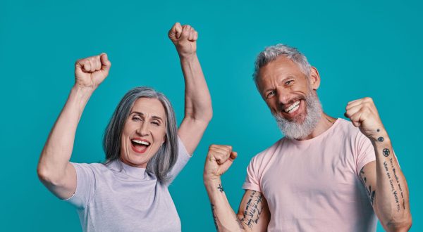 Happy senior couple looking at camera and gesturing while standing together against blue background
