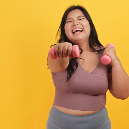 A chubby Asian woman wearing exercise clothes is showing off her physical strength on a yellow background.