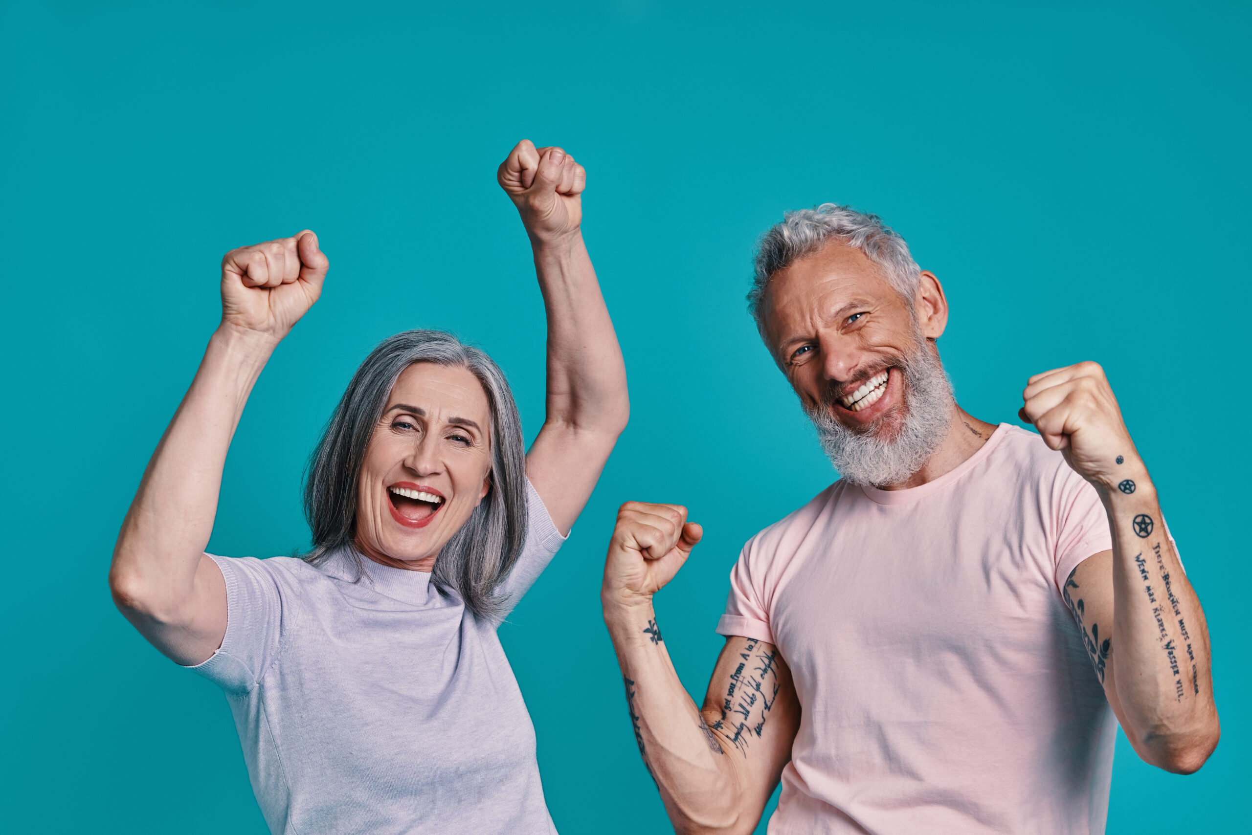 Happy senior couple looking at camera and gesturing while standing together against blue background